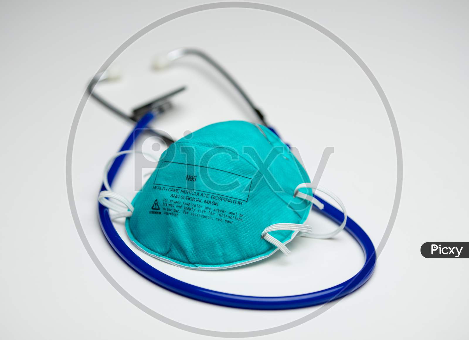 An Single Teal N95 Respirator Mask On Top Of A Blue Medical Stethoscope. Isolated On A White Background.