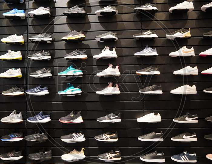 Shop Display Of A Lot Of Sports Shoes On A Wall. A View Of A Wall Of Shoes Inside The Store. Modern New Stylish Sneakers Running Shoes For Men And Women - India
