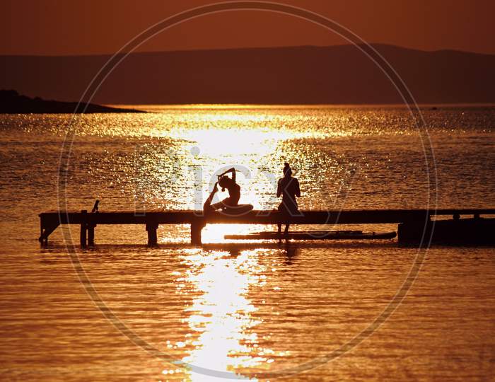 Two girls on bank over sea watertable in golden glow of sunset practicing yoga