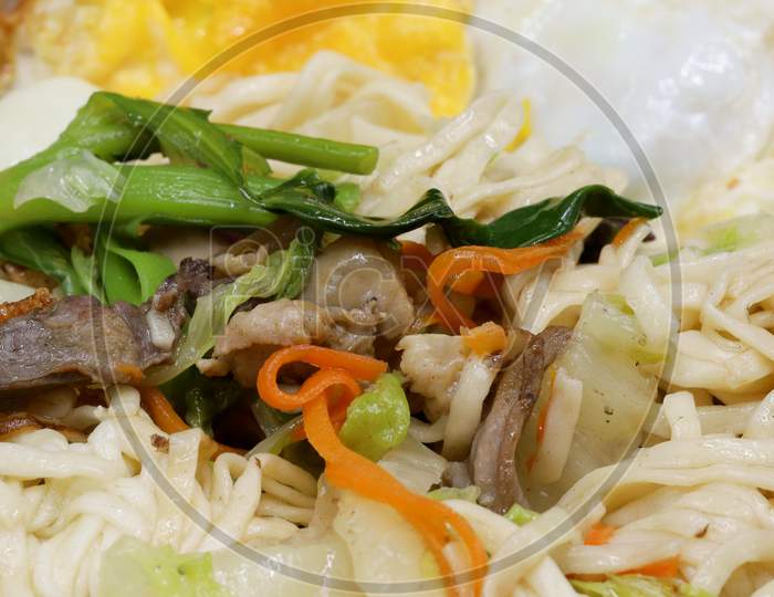 Asian vegetarian food udon noodles with Beijing cabbage, carrots, green beans, bell pepper, onions on a plate on a stone background