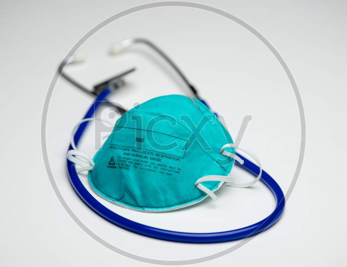 An Single Teal N95 Respirator Mask On Top Of A Blue Medical Stethoscope. Isolated On A White Background.