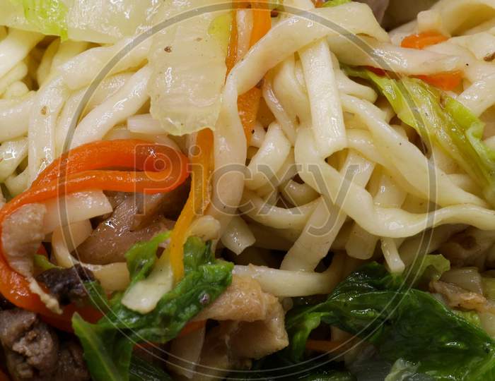 Asian vegetarian food udon noodles with Beijing cabbage, carrots, green beans, bell pepper, onions on a plate on a stone background