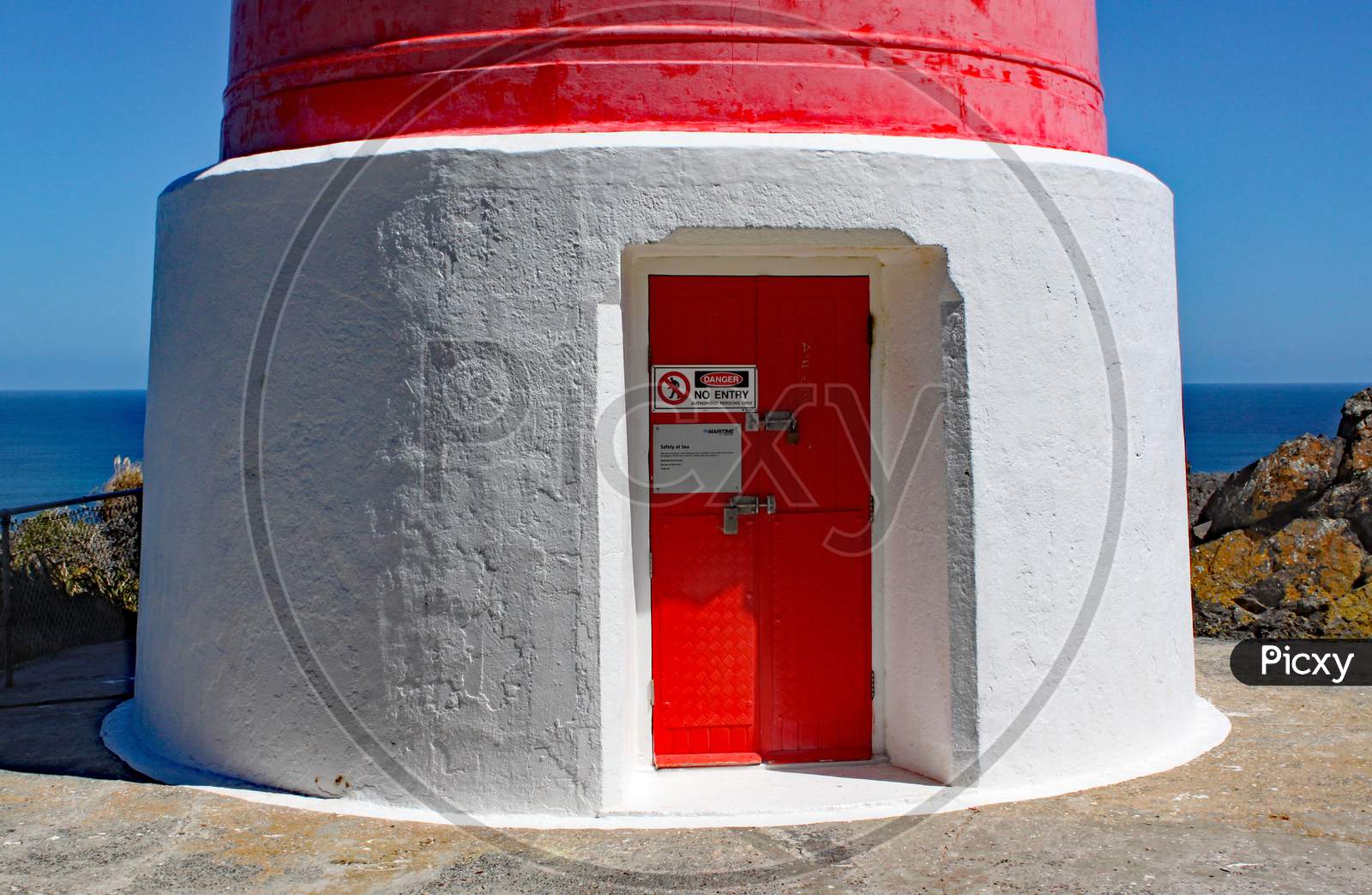 The Entrance Door Of The Red And White Striped Lighthouse At Cape Palliser On North Island, New Zealand. The Lighthouse Was Built In 1897 And Was Originally Fueled By Oil.