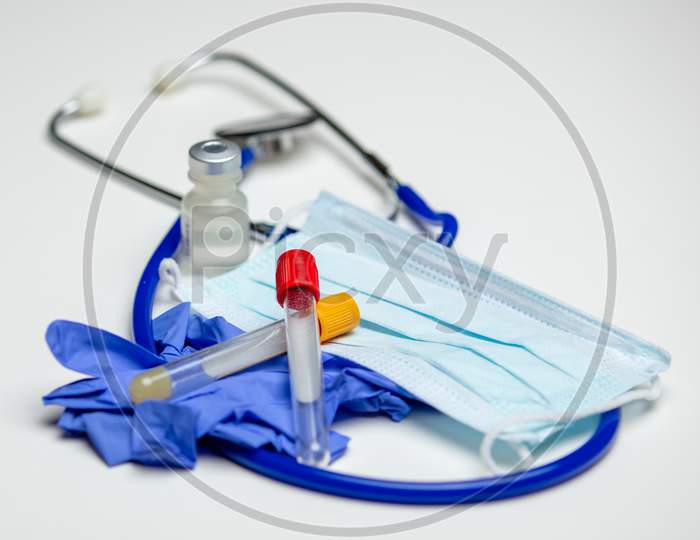 A Sterile, Empty Pair Of Glass Blood Collection Tubes Laying On Top Of A Pair Of Surgical Gloves And Mask. Stethoscope And Vial In Background.