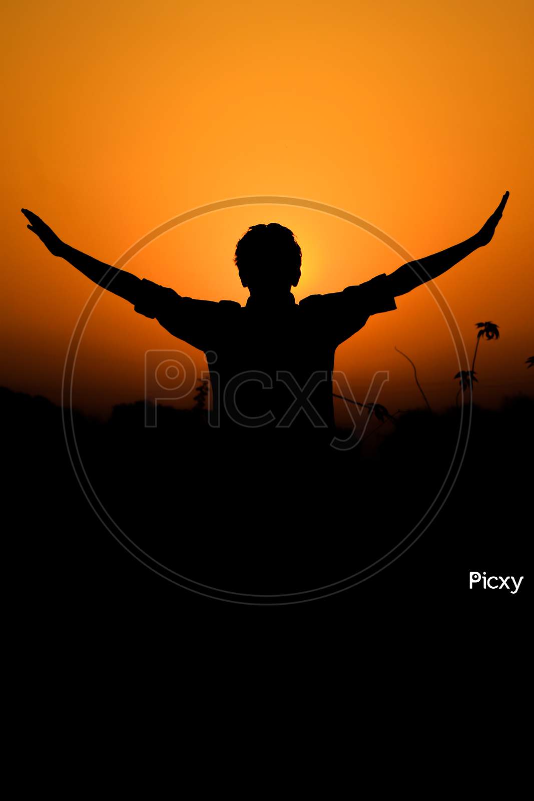 silhouette of a boy standing against setting sun with his hands spread away in joy