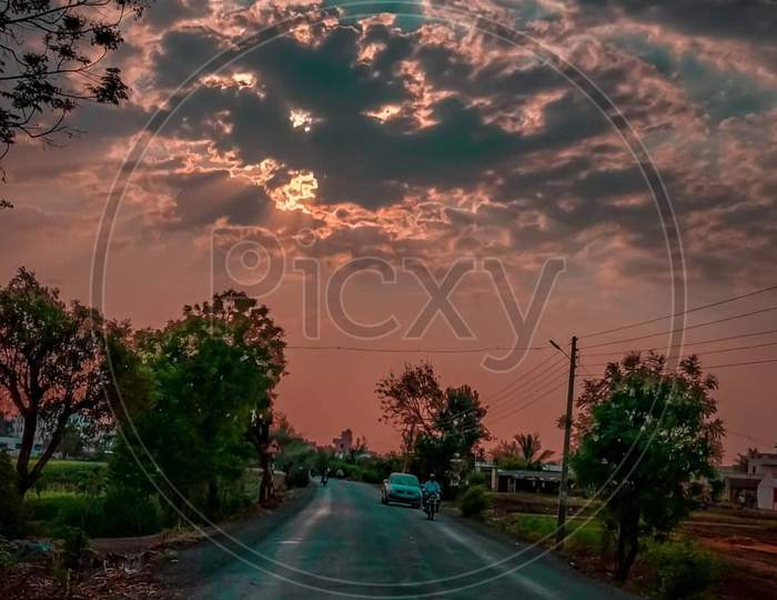 Cloudy evening with clouds covering sun and car going on road