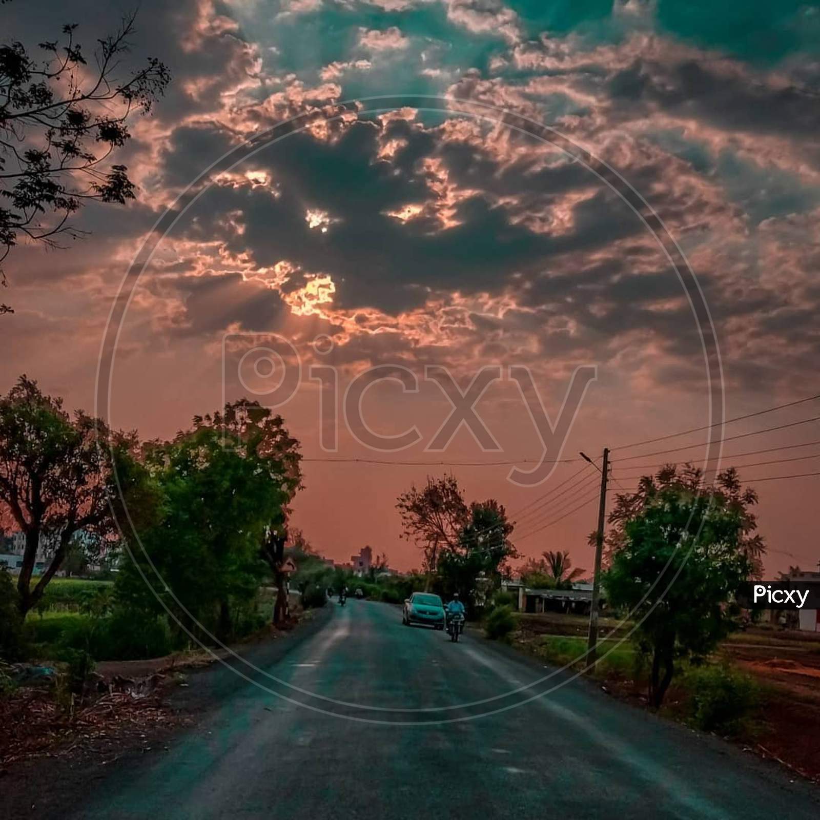 Cloudy evening with clouds covering sun and car going on road