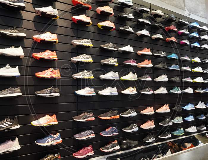 Shop Display Of A Lot Of Sports Shoes On A Wall. A View Of A Wall Of Shoes Inside The Store. Modern New Stylish Sneakers Running Shoes For Men And Women - India