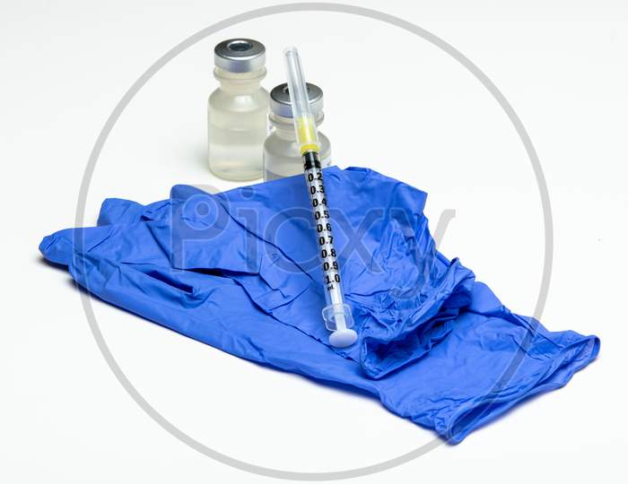 An Empty Syringe Sits On Top Of A Pair Of Gloves And Medical Vials.