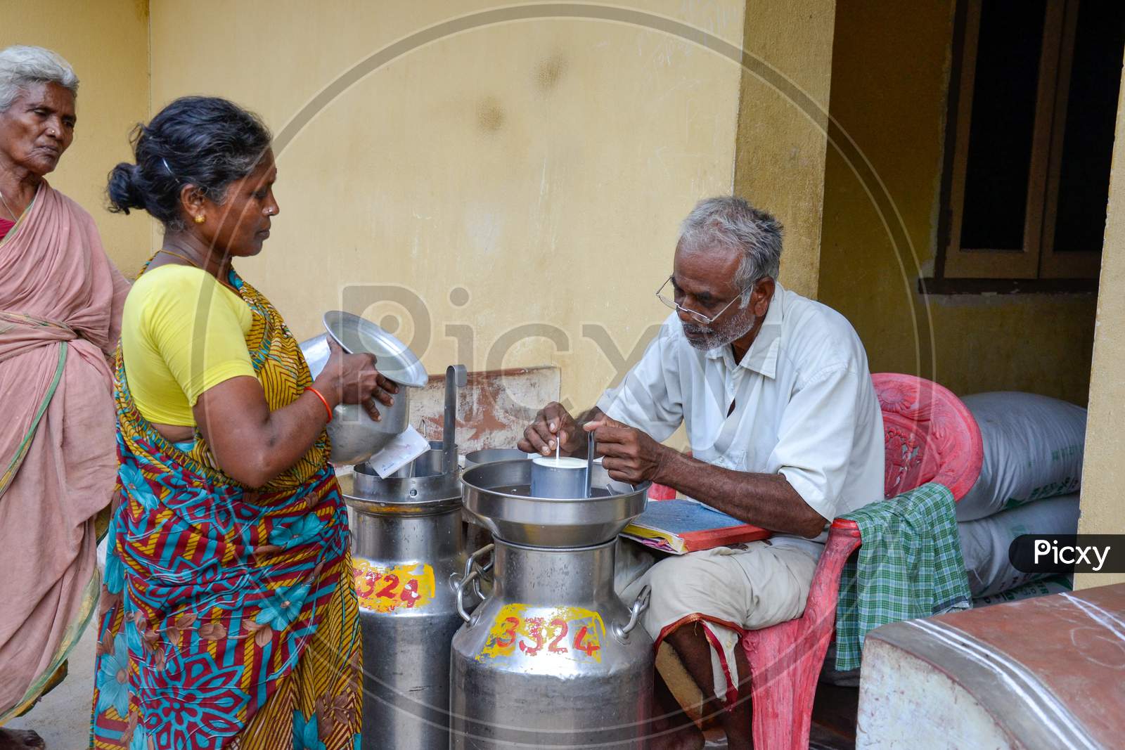 INDIA, ANDHRA PRADESH, TIRUPATI -  JUNE 2019, Rural woman in southern India pouring milk at a milk pooling point, while the collection supervisor records the quantity of the milk & do the testing.