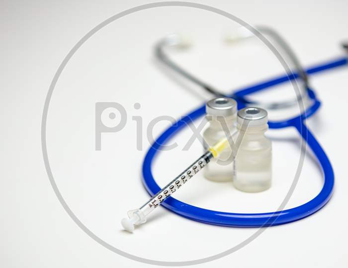 An Empty Syringe On Two Medical Vials With A Blue Stethoscope In The Background.