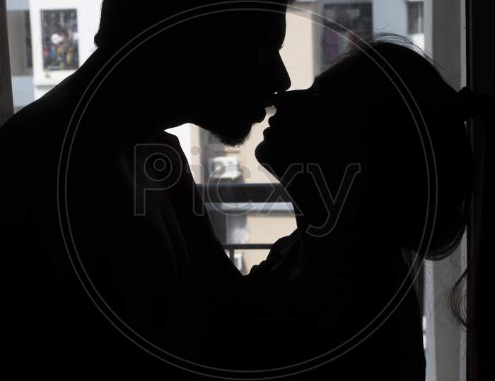 Silhouette of an Indian romantic couple kissing in front of a window. Intimate couple lifestyle