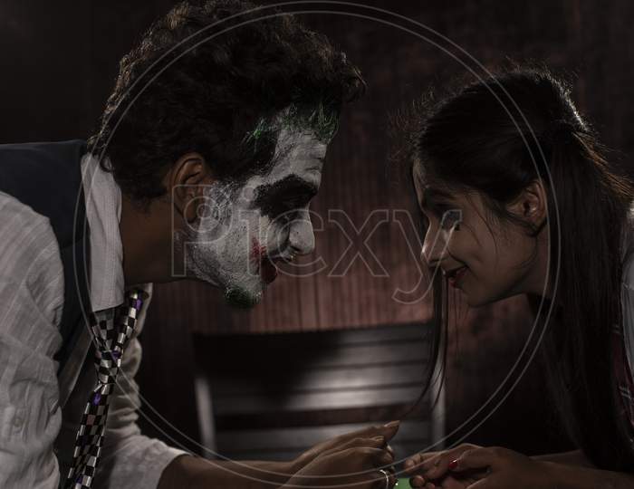 Portrait of an Indian couple in Halloween Joker costume posing on a casino poker table in textured studio background. Cosplay photography.