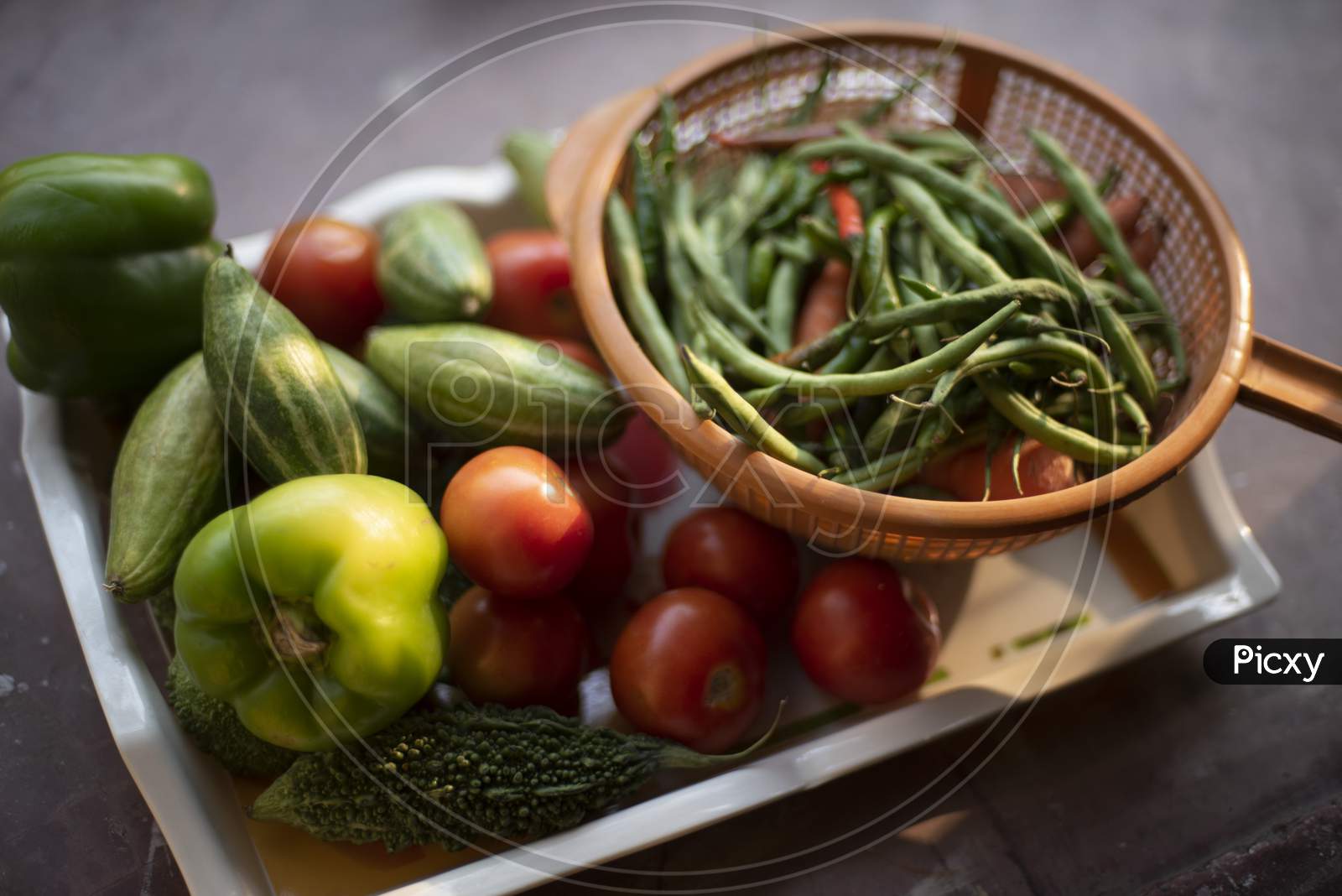 Fresh vegetables are piled up on a trey and small basket near a window with green natural background. Food, vegetables, home isolation and quarantine