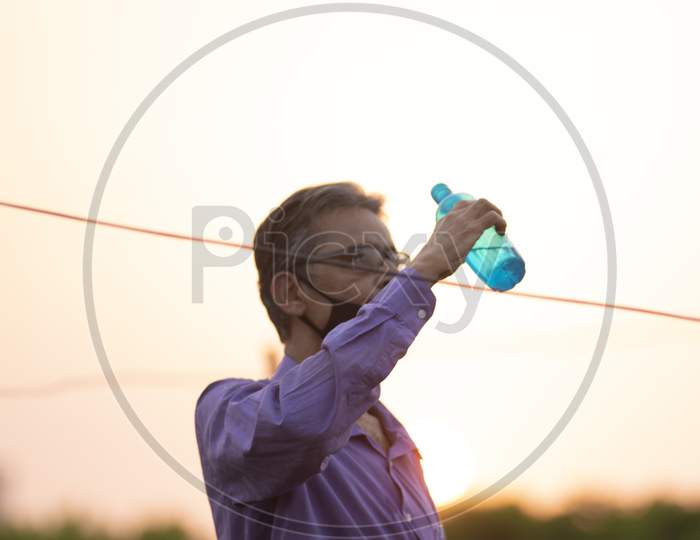 Portrait of an Indian old man with corona preventive mask drinking water from a bottle on a rooftop  in home isolation.Indian lifestyle, disease and home quarantine.
