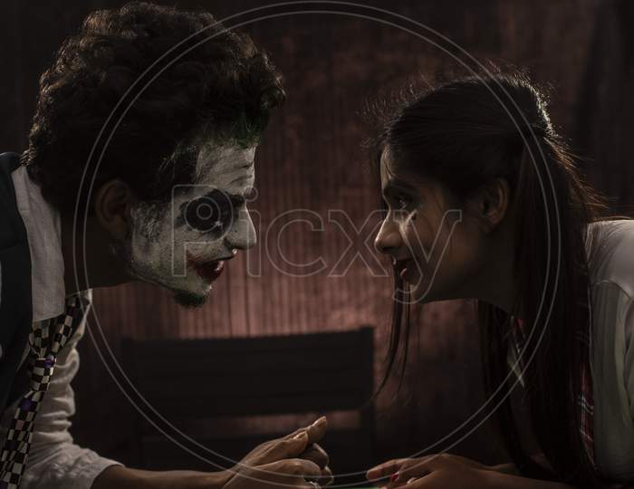 Portrait of an Indian couple in Halloween Joker costume posing on a casino poker table in textured studio background. Cosplay photography.