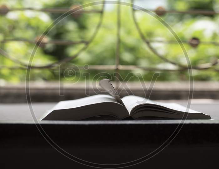 A book is kept open in front of a window with a page mark in a green background.