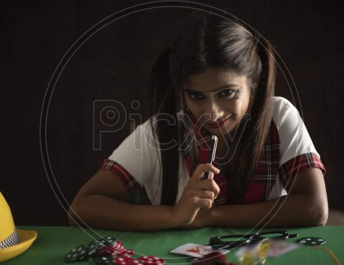 Young Indian Bengali brunette woman in school uniform with a pen playing cards on a casino poker table in brown textured copy space studio background. Indian lifestyle and fashion.