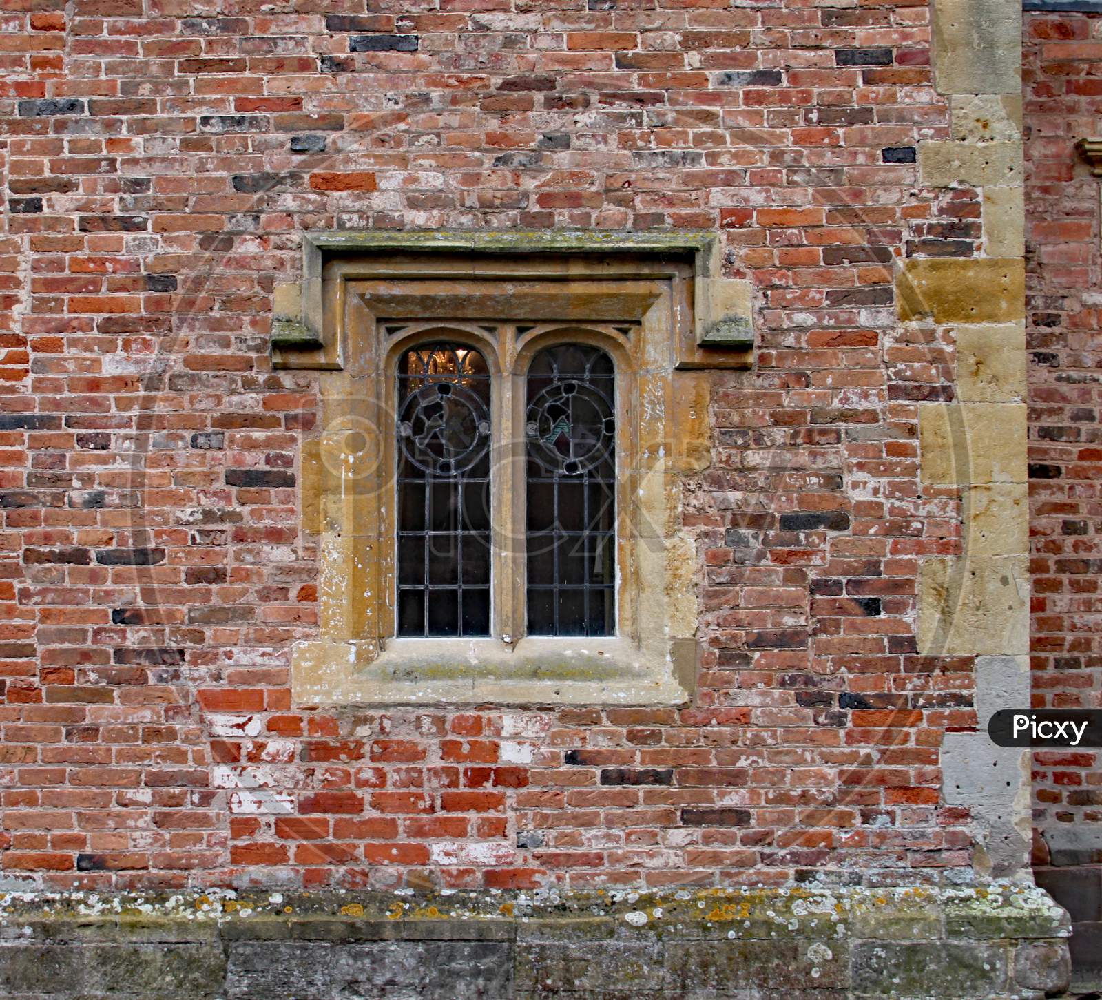 Old Ornate Concrete Window With Stained Glass In A Weathered Brick Wall In An Old Manor House