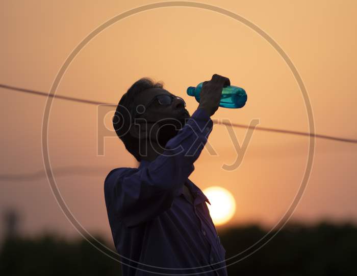 Silhouette portrait of an Indian old man with corona preventive mask drinking water on a rooftop during sunset in home isolation.Indian lifestyle, disease and home quarantine.