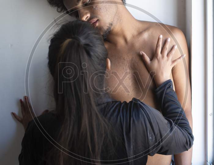 Portrait of an Indian romantic couple kissing and making love to each other standing in front of a window daytime. Intimate couple lifestyle