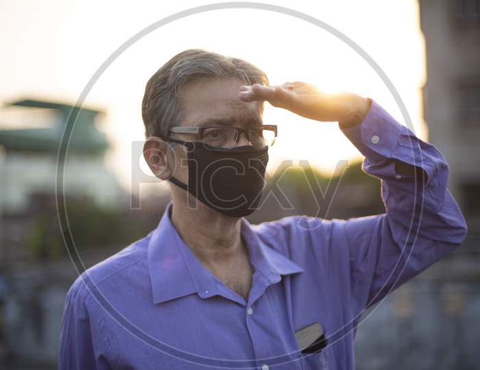 portrait of an Indian old man with corona preventive mask on a rooftop during sunset in home isolation.Indian lifestyle, disease and home quarantine.