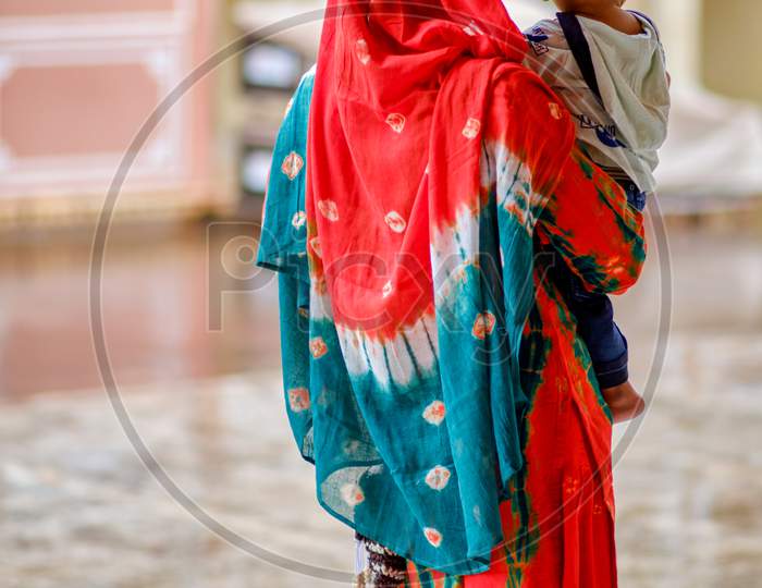 Young Rajasthani Indian Woman In Colorful Traditional Sari Holding A Baby In Jaipur (Pink City), Rajasthan, India