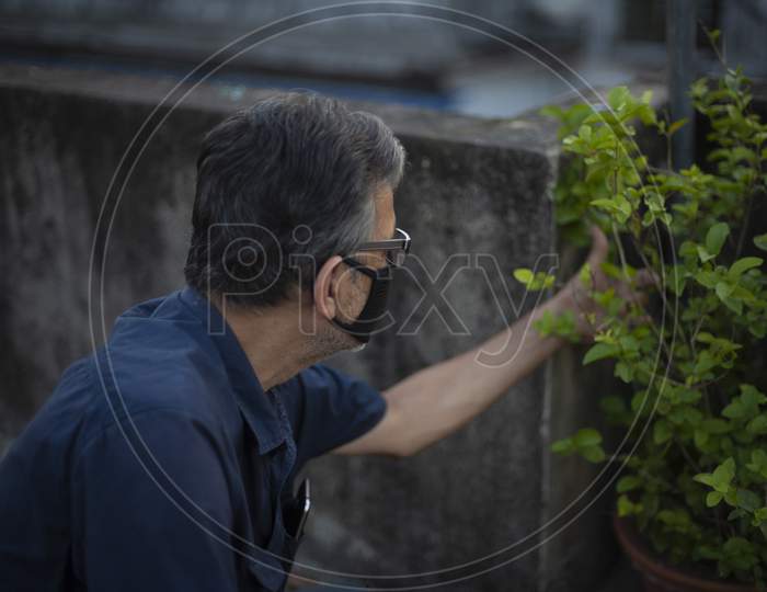 Portrait of an Indian old man wearing corona preventive mask gardening on the rooftop in home isolation. Indian lifestyle, disease and home quaratine.