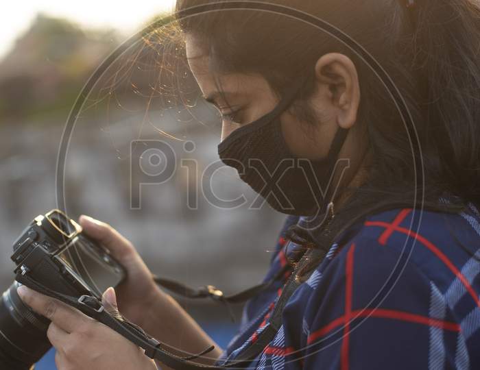 Portrait of an Indian young woman with corona preventive mask taking photograph in back light on a rooftop in home isolation.Indian lifestyle, disease and home quarantine.