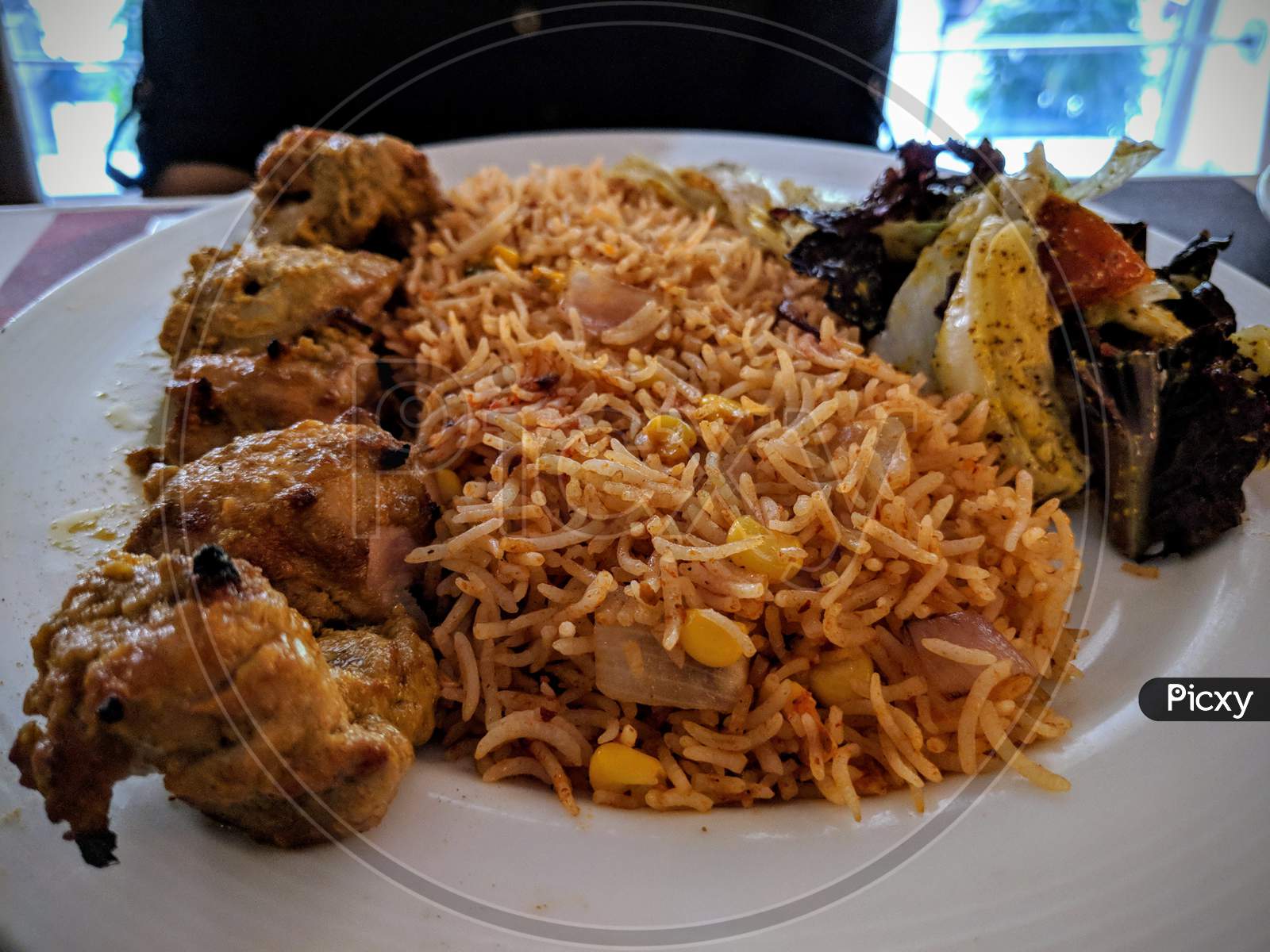 Tandoori kebab chicken with schezwan corn rice,A continental dish served on white plate with well garnish