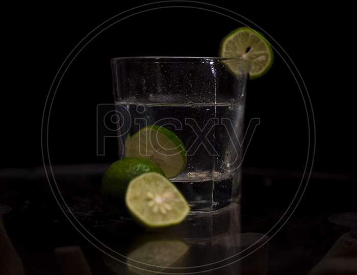 Fresh green lemon slices are immersed into a glass of water and garnished with slices of lemons in a dark copy space background.
