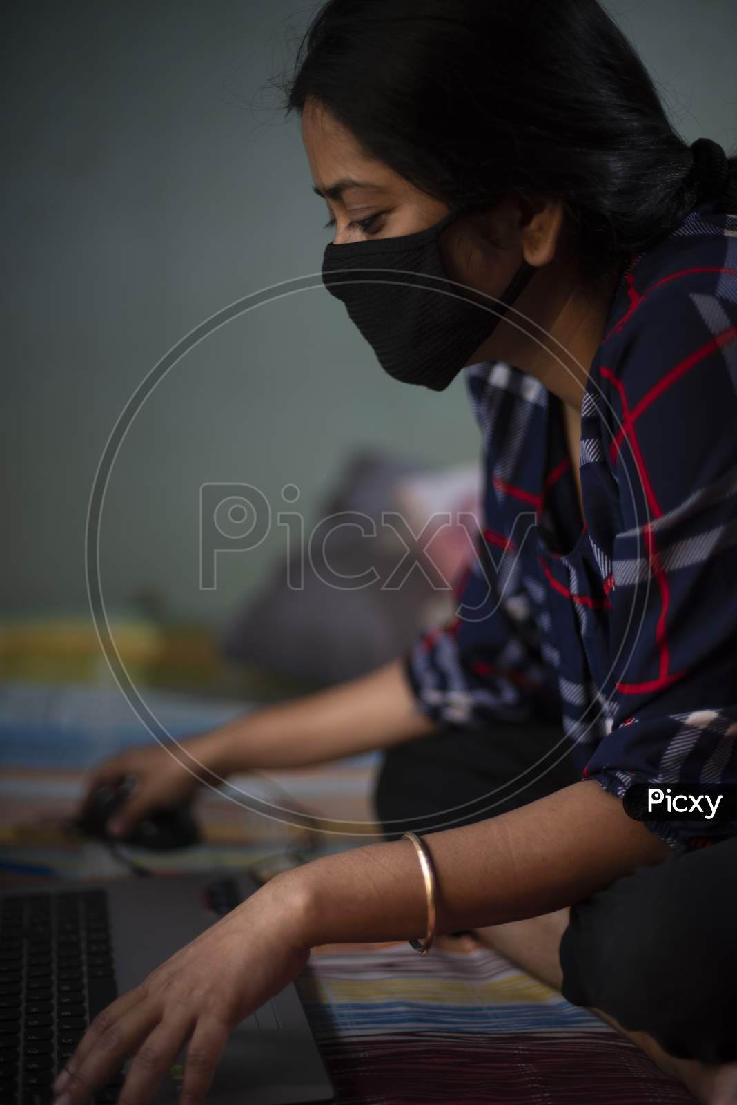 Portrait of an Indian young woman with Corona preventive mask sitting at home with a laptop home isolation due to covid - 19. Indian lifestyle and disease.