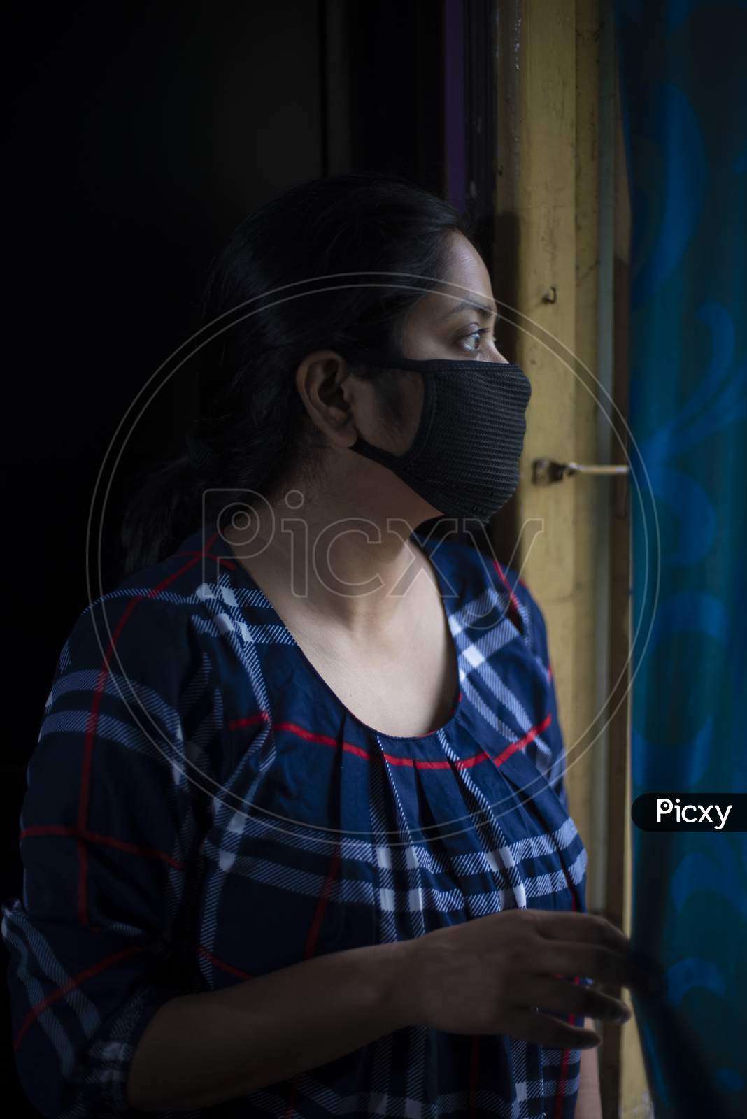 Portrait of an Indian young woman wearing corona preventive mask in home isolation in front of a window. Indian lifestyle and disease.