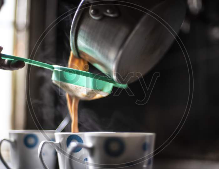 Tea being strained and poured into the cups from an aluminium tea pot in an Indian kitchen. Indian drink and beverages.