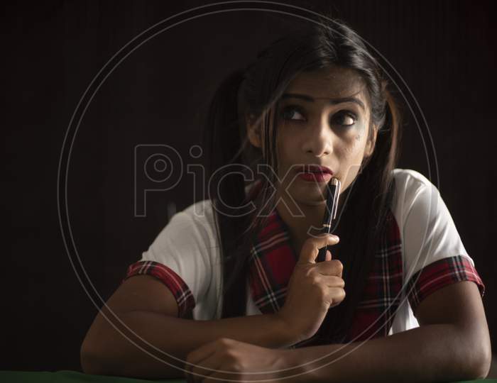 Young Indian Bengali brunette woman in school uniform with a pen playing cards on a casino poker table in brown textured copy space studio background. Indian lifestyle and fashion.