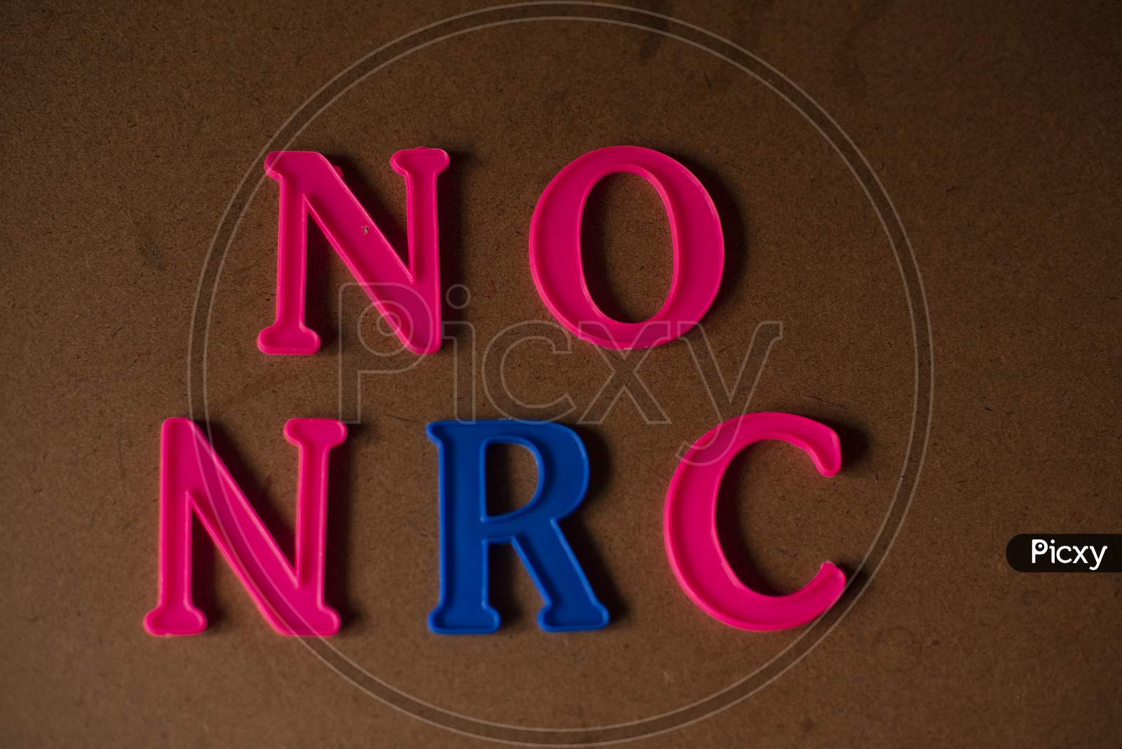 'NO NRC' written on a brown wooden background with lines of shadow.