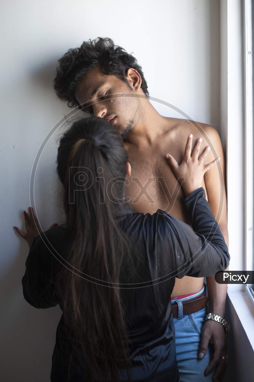 Portrait of an Indian romantic couple kissing and making love to each other standing in front of a window daytime. Intimate couple lifestyle