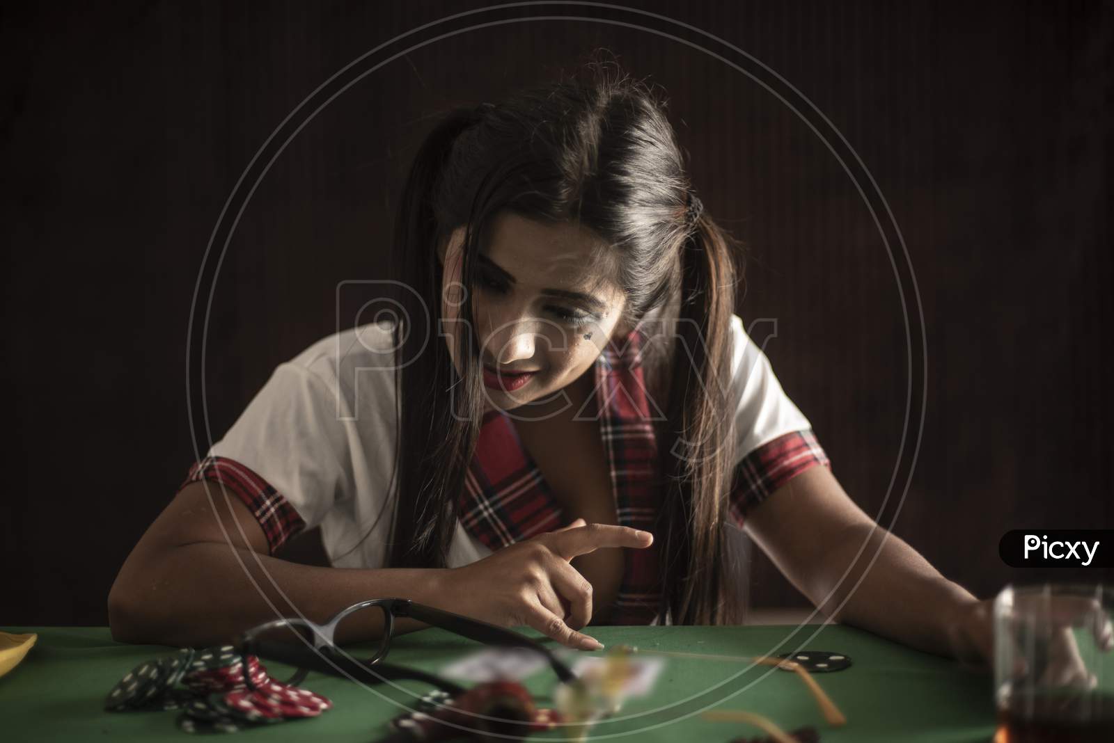 Young Indian Bengali brunette woman in school uniform playing cards on a casino poker table in brown textured copy space studio background. Indian lifestyle and fashion.