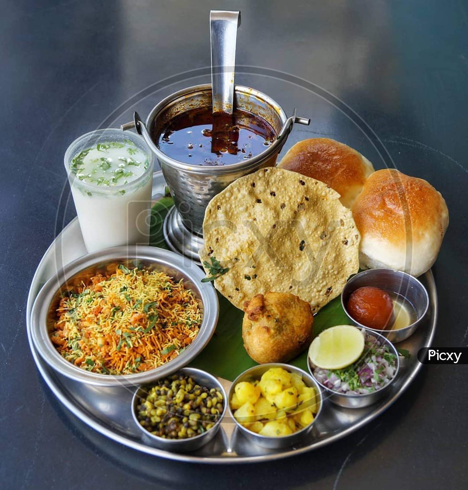 Misal thali served with bread buttermilk pappad onion and several ingredients