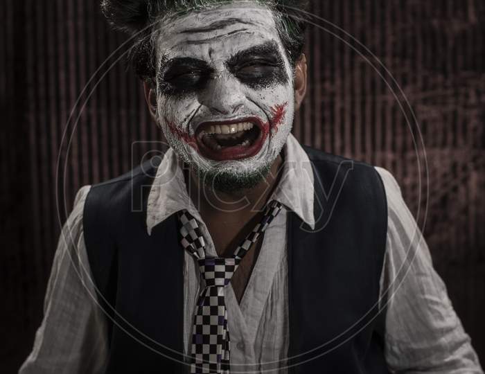 Portrait of an Indian man in Joker Halloween costume showing scary facial expression in front of a casino poker table. Cosplay photography.