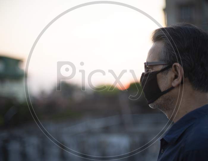 Side portrait of an Indian old man wearing corona preventive mask on a rooftop  in home isolation.Indian lifestyle, disease and home quarantine.
