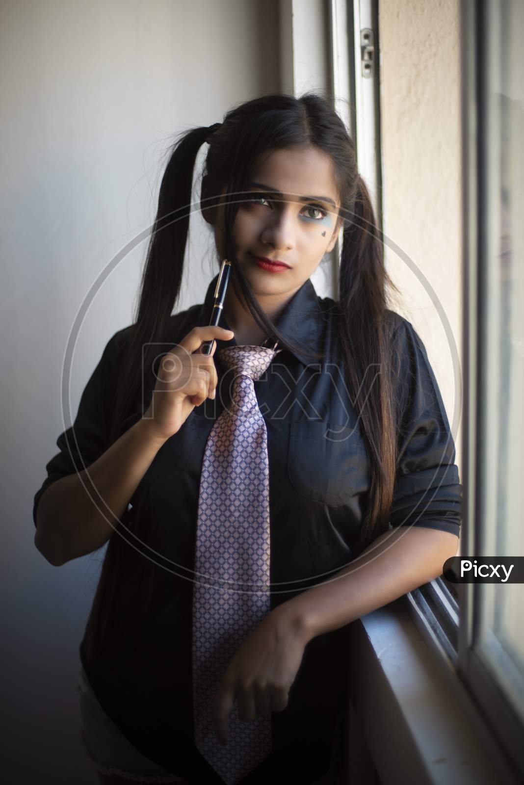 Portrait of an young Indian brunette girl in black corporate suit with spectacles and pen in front of a glass window in white background. Indian lifestyle and corporate
