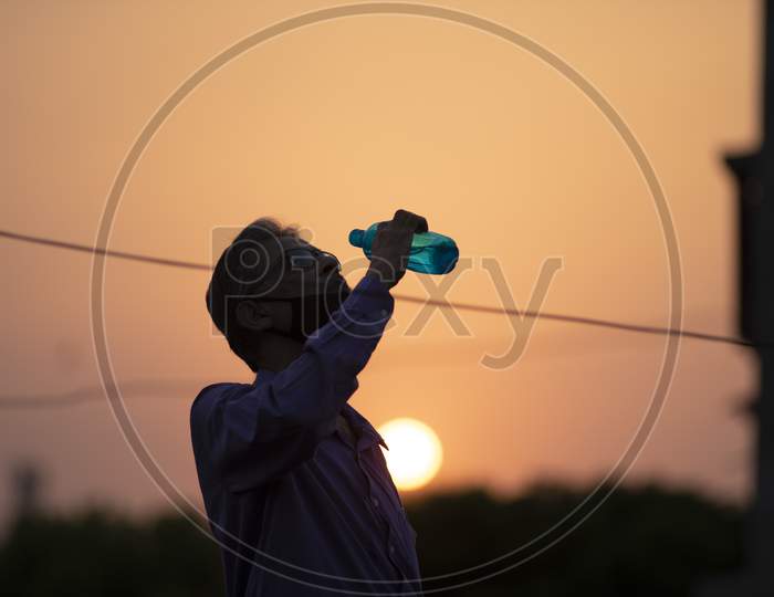Silhouette portrait of an Indian old man with corona preventive mask drinking water on a rooftop during sunset in home isolation.Indian lifestyle, disease and home quarantine.