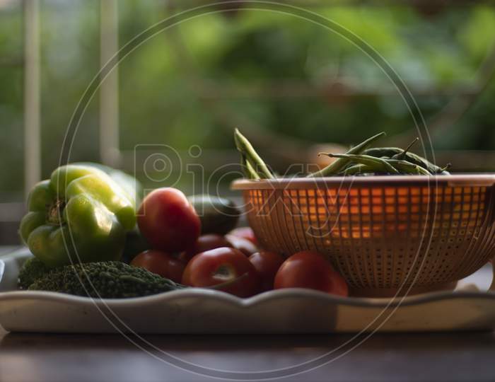 Fresh vegetables are piled up on a trey and small basket near a window with green natural background. Food, vegetables, home isolation and quarantine