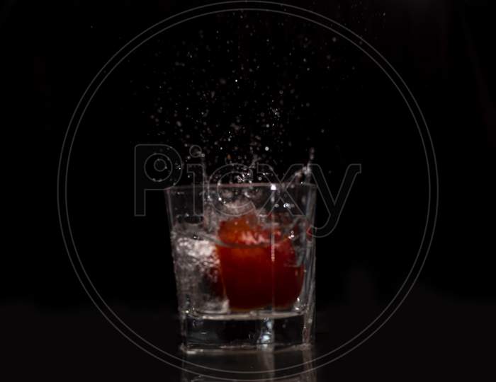 Water splashing out from a glass due to the immersion of a fresh red tomato into it.