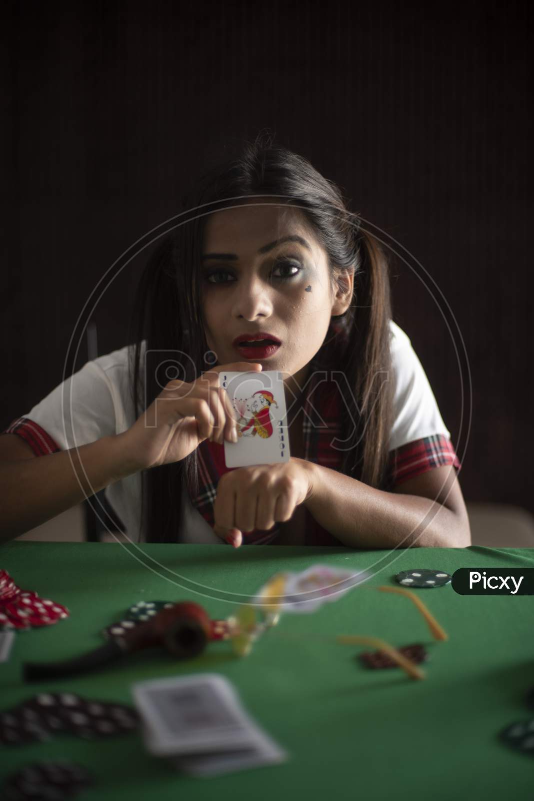 Young Indian Bengali brunette woman in school uniform playing cards on a casino poker table in brown textured copy space studio background. Indian lifestyle and fashion.