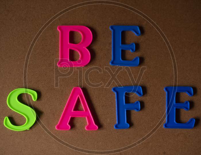 'BE SAFE' written on a brown wooden background with lines of shadow.