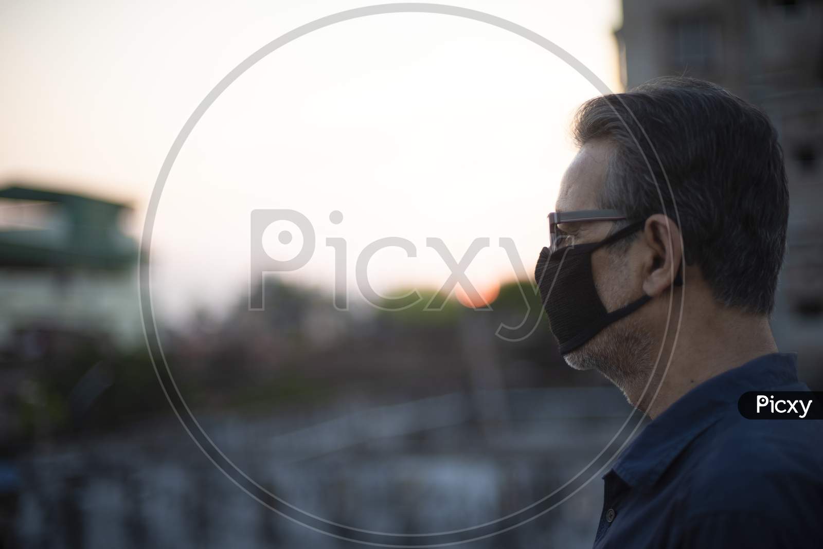 Side portrait of an Indian old man wearing corona preventive mask on a rooftop  in home isolation.Indian lifestyle, disease and home quarantine.