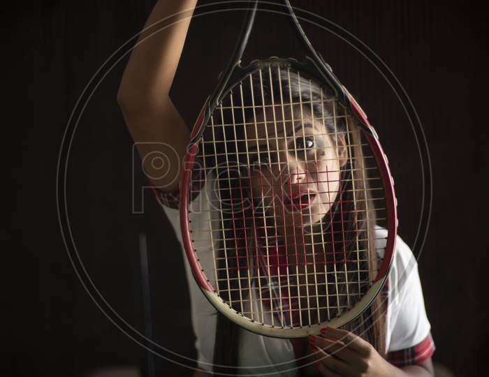 Young Indian Bengali brunette woman in school uniform with a tennis racket sitting on a casino poker table in brown textured copy space studio background. Indian lifestyle and fashion.