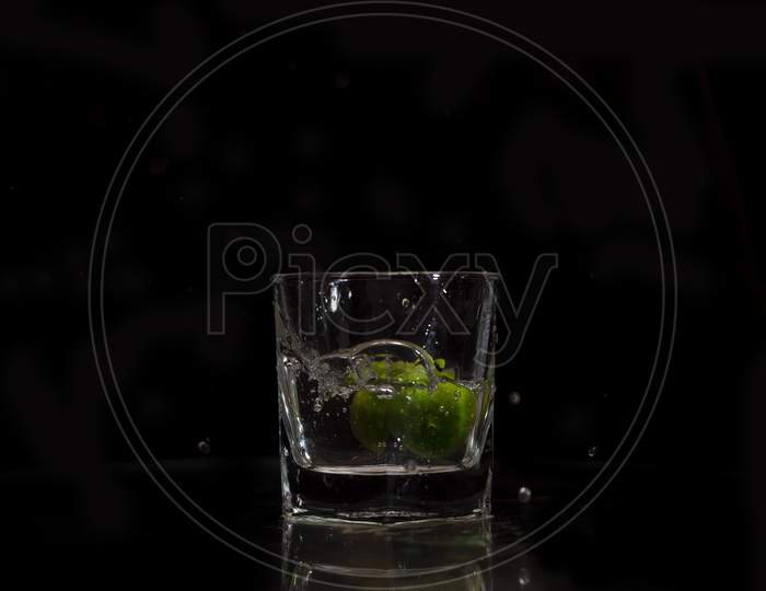 Water splashing out from a glass due to the immersion of a fresh green small lime into it.